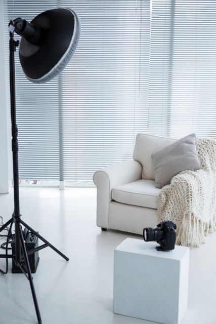This image shows a modern photostudio with a white armchair, a spotlight, and a camera on a pedestal. The setting is minimalistic and professional, ideal for use in articles or advertisements related to photography, studio setups, or creative workspaces. It can also be used in blogs or websites focusing on interior design or professional equipment.
