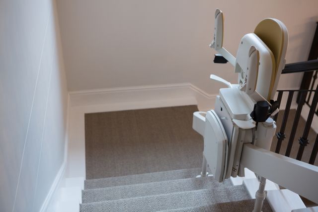 Close-up view of a stairlift installed on a staircase railing in a modern home. Ideal for illustrating concepts of accessibility, elderly care, and mobility aids. Useful for articles, brochures, and websites focused on home modifications, safety, and independence for the elderly or disabled.