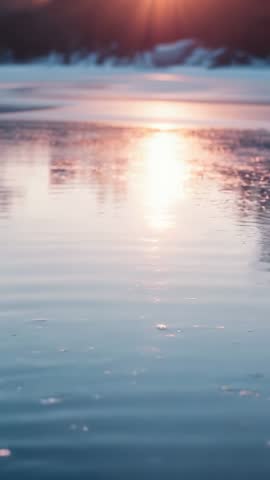Vertical sun rising melting ice creating gentle ripples and golden reflection at dawn