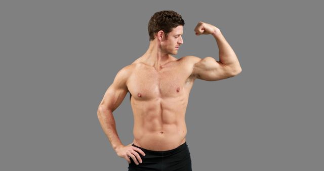 A young Caucasian man showcases his muscular physique by flexing his bicep, with copy space. His confident pose and well-defined muscles emphasize a focus on fitness and strength.