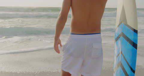 Young Man with Surfboard Facing Ocean Waves at Beach