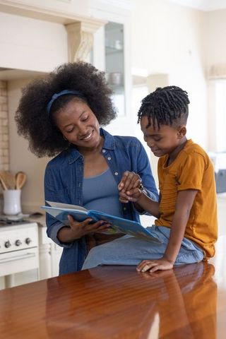 African american mother reading picture book with son at kitchen island sharing moment