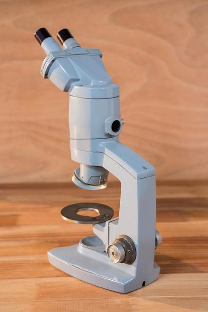 Close-up of a microscope placed on a wooden table. Ideal for use in educational materials, scientific research articles, laboratory equipment catalogs, and healthcare-related content. Highlights the precision and importance of scientific instruments in research and education.