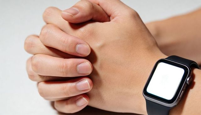 Hands clasping and wearing smartwatch with blank screen closeup on light tabletop