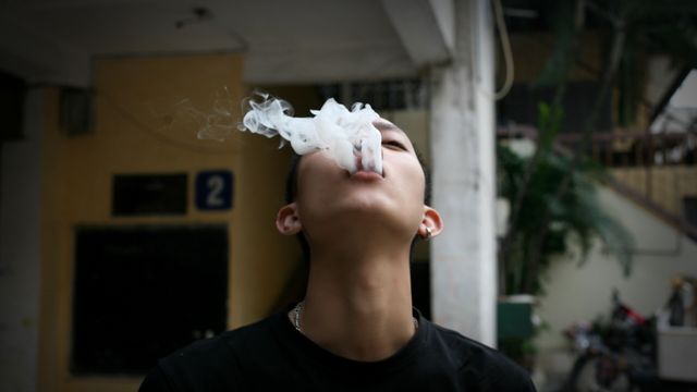 Youth exhaling smoke from their mouth in an outdoor urban environment, showing effects of smoking. Useful for projects concerning health awareness, youth culture, rebellion, and anti-smoking campaigns.