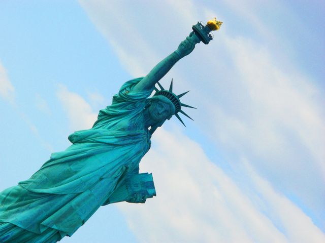Iconic Statue of Liberty against a cloudy sky, displaying the torch and tablet. Ideal for travel guides, patriotic themes, educational materials, and promotions related to New York City tourism.