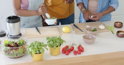 African family preparing fresh salad together in bright modern kitchen with basil pots