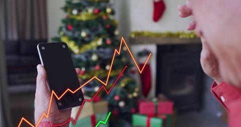 Senior holding smartphone with holiday tree, gifts and volatile financial graph overlay