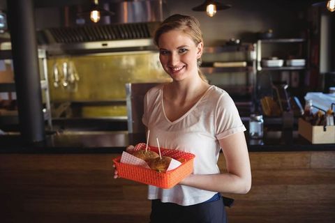 Cheerful Female Server Holding Burger Basket in Trendy Restaurant