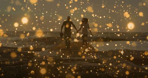 Couple walking hand in hand on jetty at sunset with golden bokeh silhouettes
