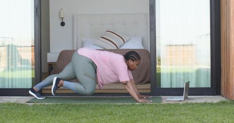 African-american woman doing outdoor core exercise in doorway following online workout