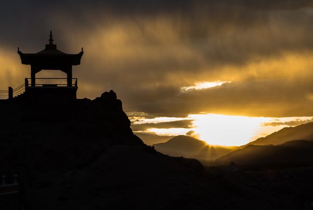 Silhouette of a peaceful pagoda perched atop a mountain during a dramatic sunset, with the sky painted in golden hues. Ideal for travel brochures, meditation concepts, desktop wallpapers, and nature-themed designs. Perfect for conveying tranquility, serenity, and the majestic beauty of nature.