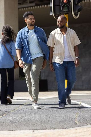 African american men and friend walking across sunlit urban crosswalk under signal