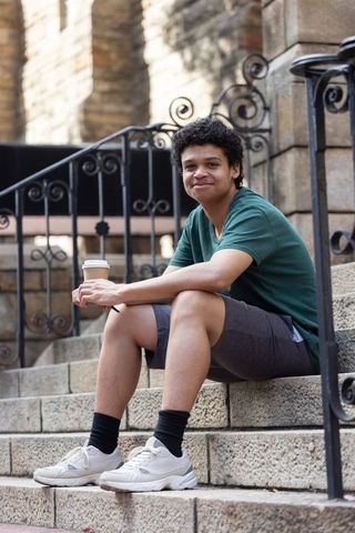 African american man relaxing on stone steps holding coffee cup by wrought-iron railings