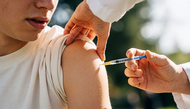 Nurse administering vaccine into upper arm outdoors in natural sunlight