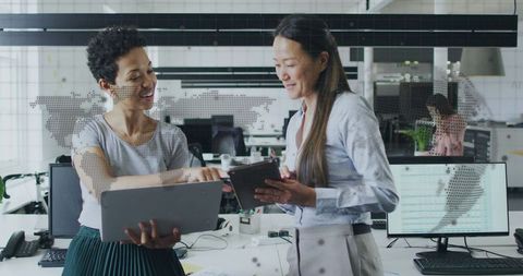 Professional women collaborating with laptop and tablet in modern open-plan office