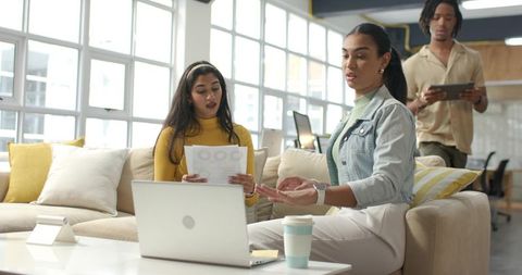 Diverse young professionals collaborating, brainstorming on couch in modern office lounge