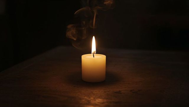 Single Burning Pillar Candle Casting Warm Amber Glow on Rustic Wooden Table at Night
