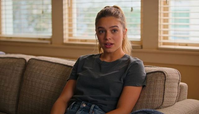 Young woman sitting on beige sofa, leaning back and talking, casual at-home conversation
