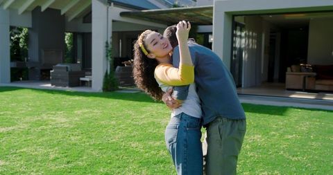 Happy Young Couple Embracing on Sunny Lawn by Modern Home