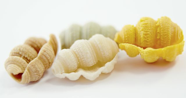 Image shows four assorted colorful pasta shells arranged on a white background in close-up. Each shell displays distinct texture and shape. Useful for food blogs, Italian cuisine promotional materials, grocery websites, or culinary magazines focusing on pasta varieties.