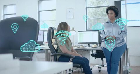 Female colleagues collaborating in modern office with holographic cloud and location icons
