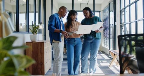 African american team collaborating on laptop in bright daylight glass office corridor