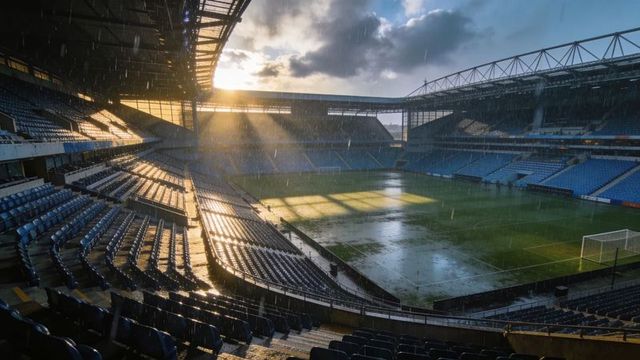 Sunbeams piercing rainy empty stadium glistening on wet pitch and blue seats