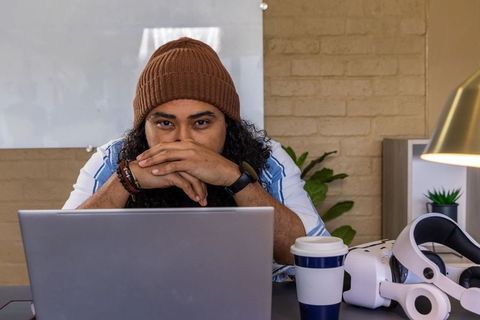 Young man wearing knit beanie working at home using laptop and vr headset in workspace