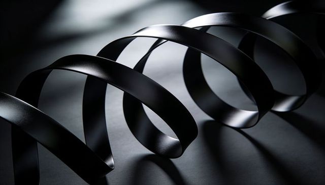 Coiling matte black metal ribbon creating sculptural spiral with dramatic highlights