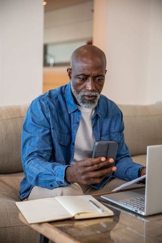Senior man at home office using smartphone and laptop
