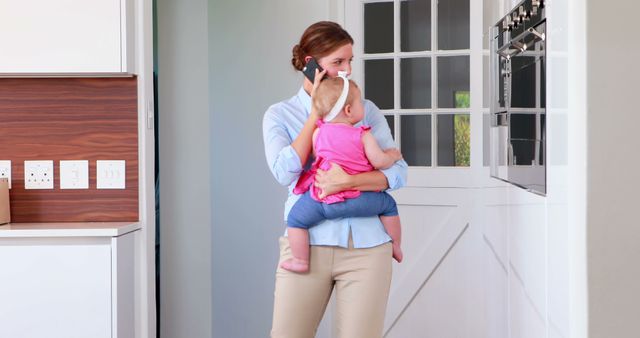 Busy Mother Holding Baby While Talking on Phone in Modern Kitchen - Download Free Stock Images Pikwizard.com