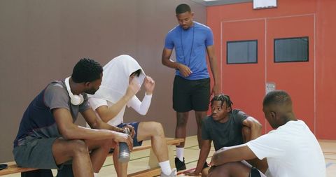 Diverse basketball players taking water break on bench with coach draping towel postgame