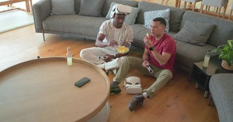 Friends playing vr games in living room with headset and controllers, snacking on floor