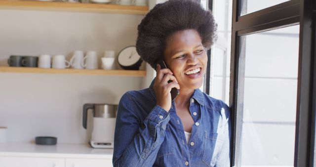 Happy african american woman talking on smartphone in kitchen. domestic lifestyle, spending free time at home.