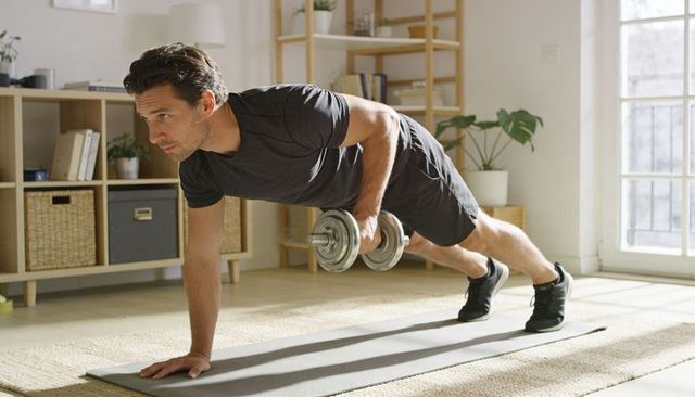 Man performing dumbbell renegade row plank on mat in sunlit minimalist living room