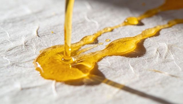Pouring amber resin forming glossy pool on fibrous paper macro closeup honeylike texture