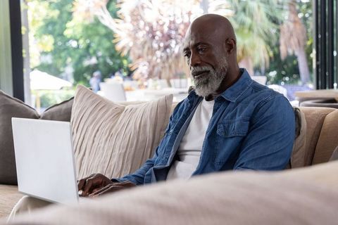 Mature african american man working on laptop in bright modern living room on sofa