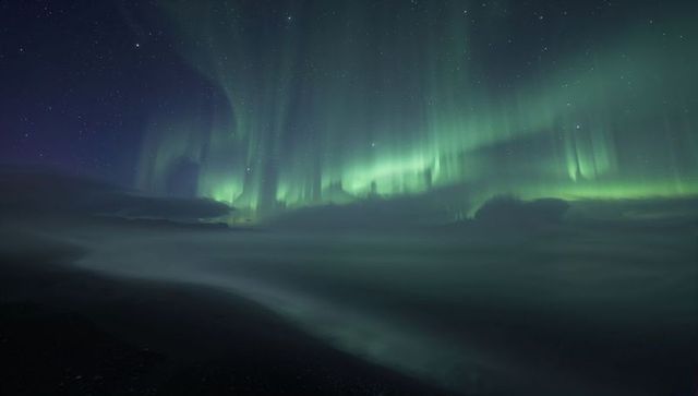 Dancing Aurora Curtains Over Misty Arctic Coastline Under Starry Night Sky