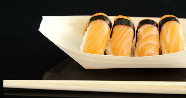A serving of salmon nigiri sushi is presented elegantly on a wooden boat-shaped plate, accompanied by chopsticks, with copy space. Sushi is a traditional Japanese dish, popular worldwide for its delicate flavors and artistic presentation.