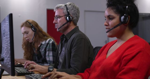 Professionals in a call center office, focused on their screens. They wear headsets, managing customer service with expertise and attention to detail.