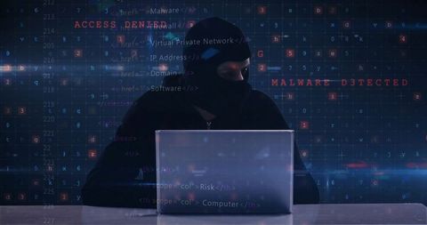 Hacker in Balaclava at Laptop Engaged in Cyberattack Activities
