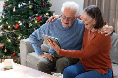 Senior Couple Enjoying Tablet Near Christmas Tree in Modern Living Room