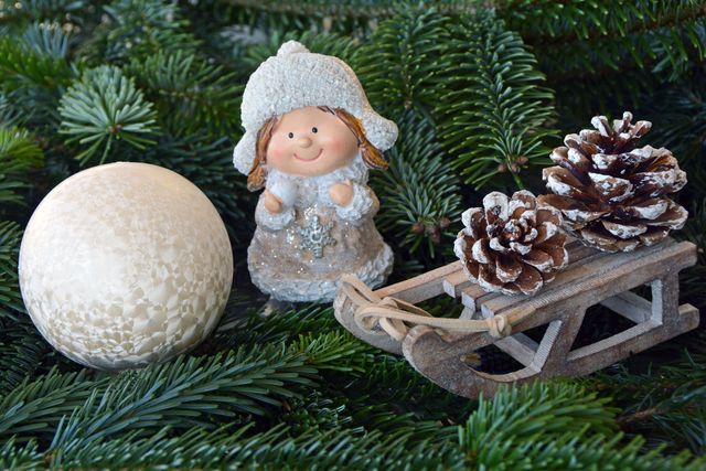 Decorative objects including a smiling angel figurine, pinecones dusted with snow, and a small wooden sleigh on Christmas greenery. Ideal for holiday greeting cards, winter-themed designs, home decor inspiration, or festive promotional material.