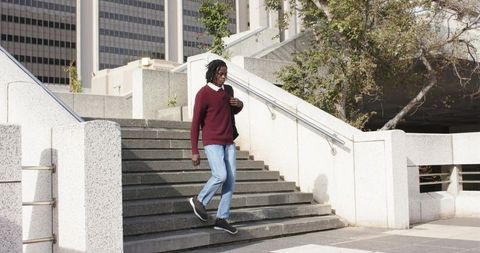 African american man walking down concrete stairs in downtown plaza carrying shoulder bag
