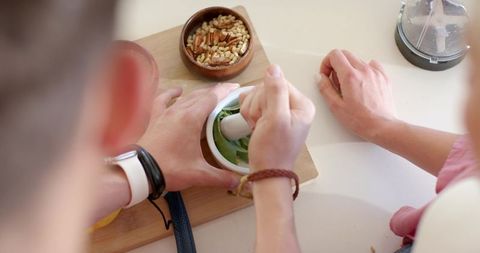 Two people crushing fresh herbs with mortar and pestle on home kitchen counter