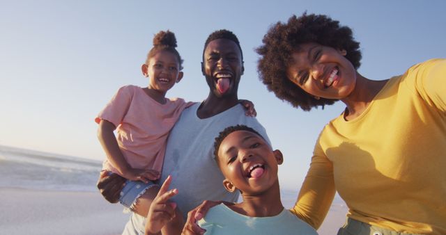 Portrait of smiling african american family looking at camera on sunny beach. healthy, active family beach holiday.