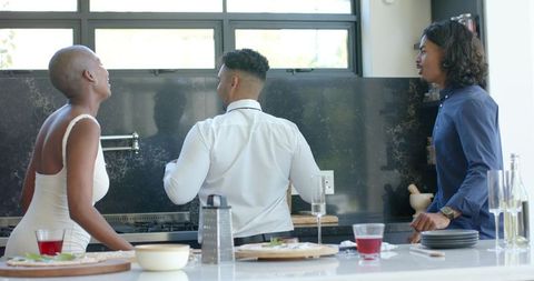 African american friends laughing and preparing food at modern kitchen island gathering