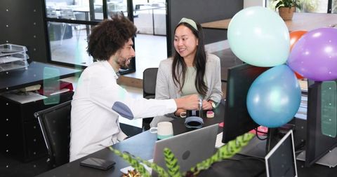 Coworkers celebrating office milestone with balloons while collaborating at desk