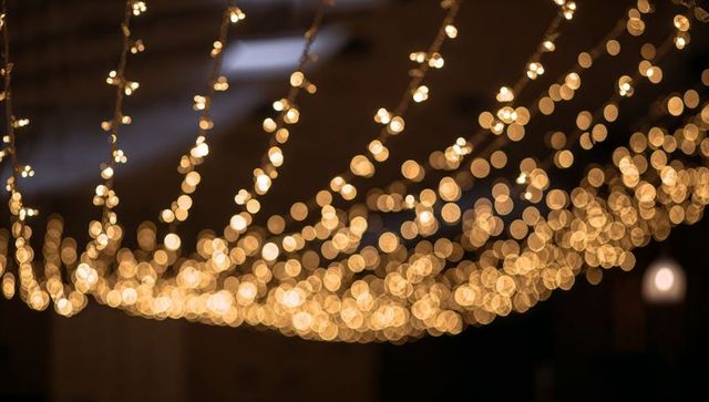 Warm bokeh canopy of hanging string lights over rustic interior venue rafters